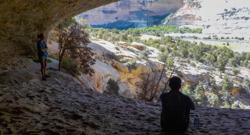 A person rests in the shade of a canyon overlooking a desert area.